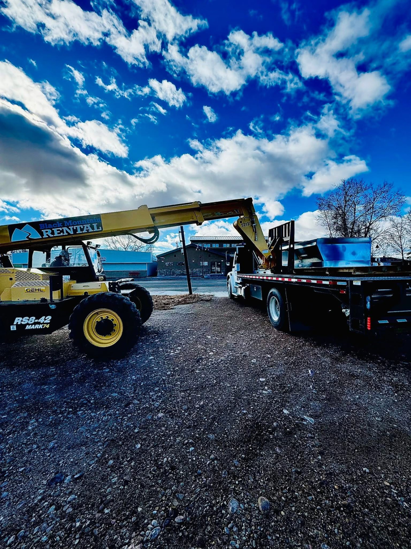 Telehandler and flatbed truck staged to set a commercial rooftop unit
